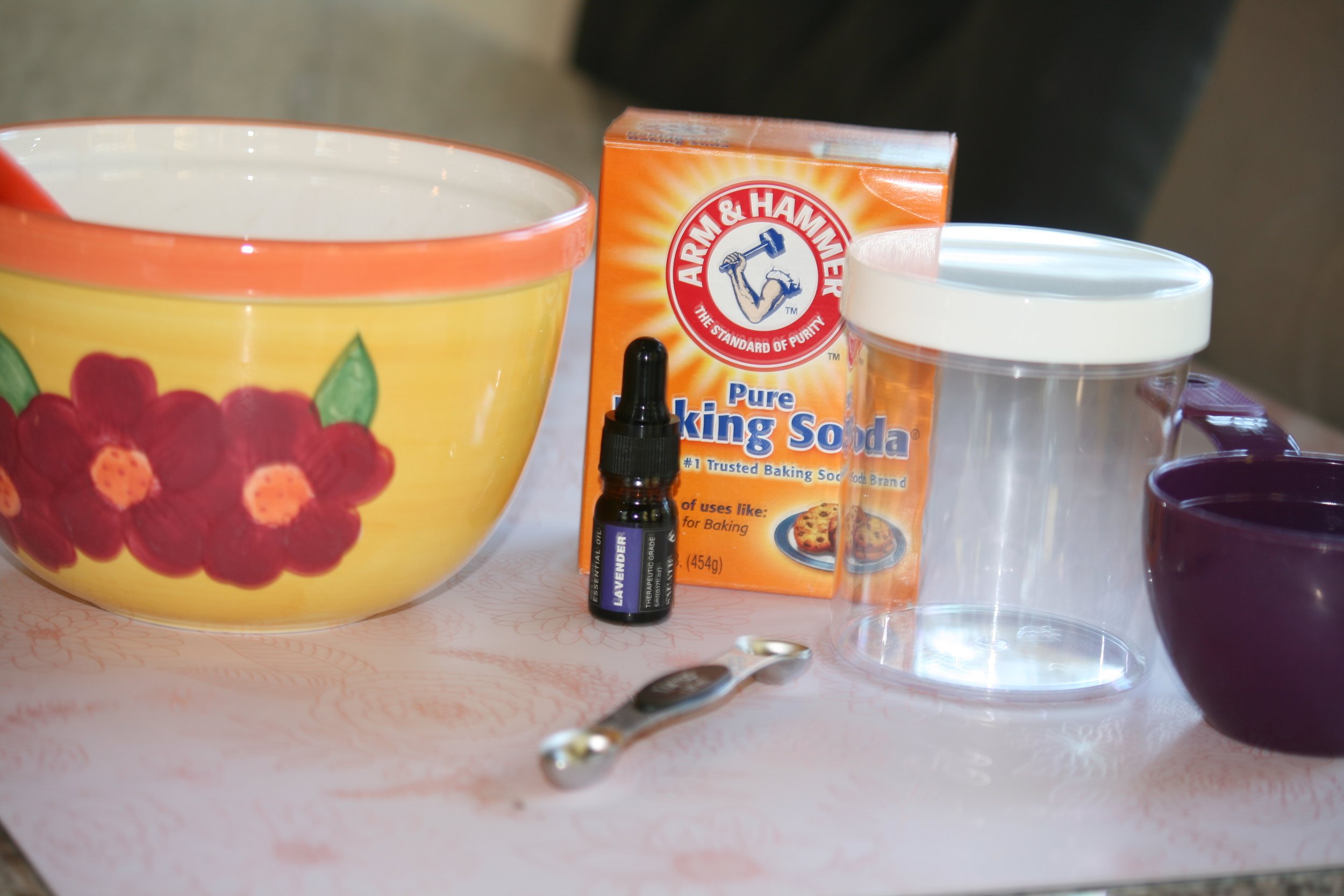 yellow mixing bowl, dropper of lavender oil, box of baking soda, measuring spoon, clear plastic container with lid