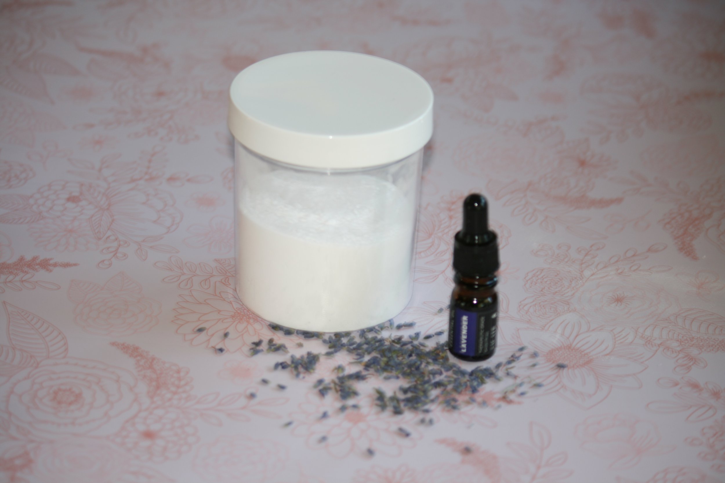 clear plastic jar containing baking soda, scattered lavender buds, amber dropper bottle with lavender oil