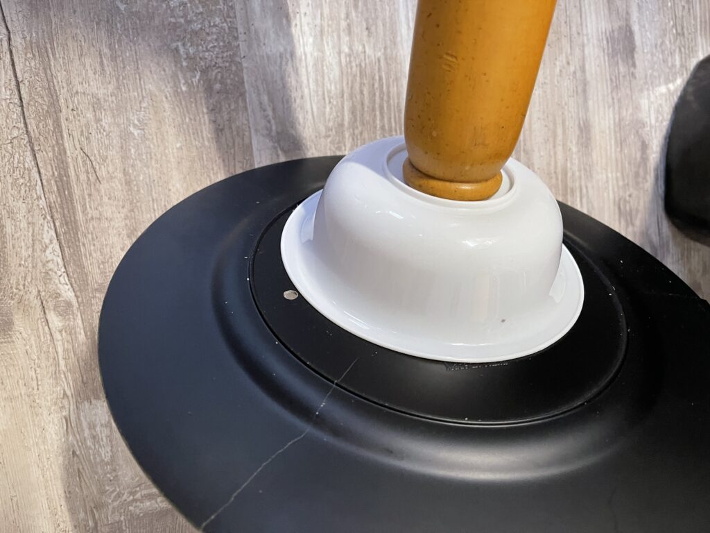 black plastic charger plate, upside down, with white bowl on tope of it and a dowel coming out of the bowl