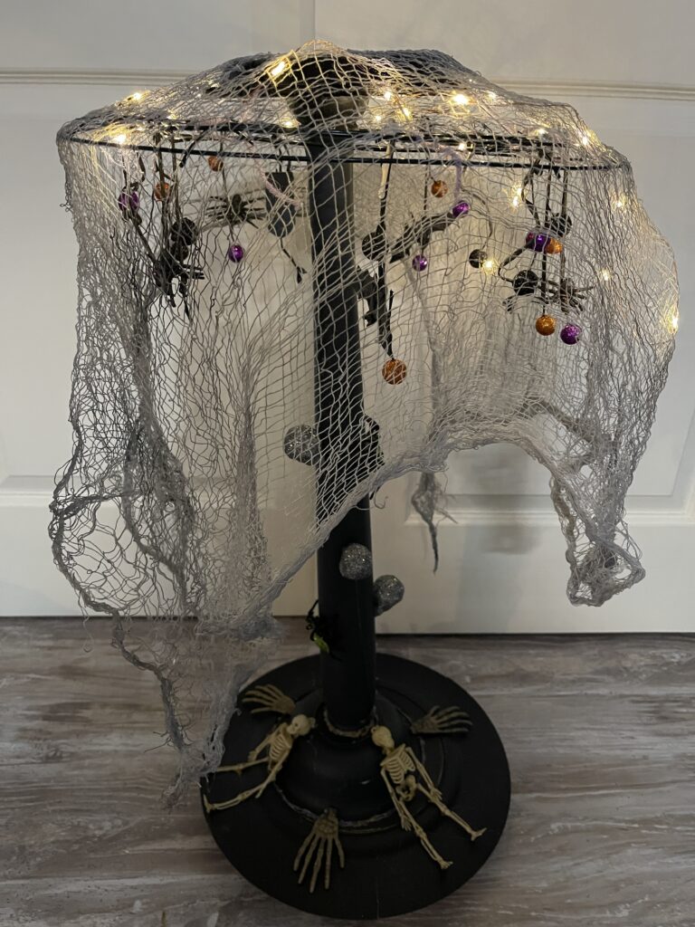 black table lamp with fairy lights, skeletons glued on it and a black cloth hung over it that looks like cheesecloth