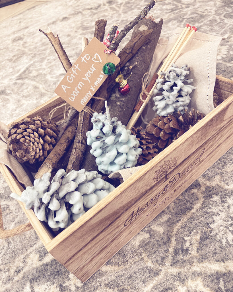 open wooden box containing a few pinecones, 3 pinecones coated in light blue wax, a bundle of sticks tied together, a few long matches