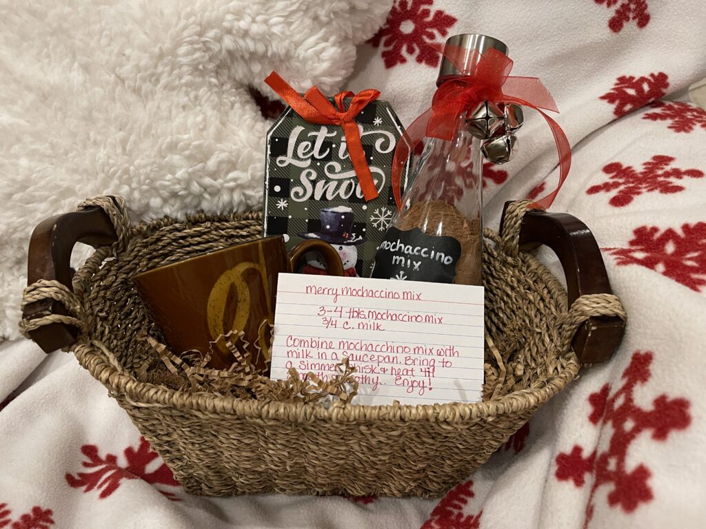 small basket containing brown coffee mug, ornament and reusable glass water bottle with mocha hot drink mix in it and recipe on top
