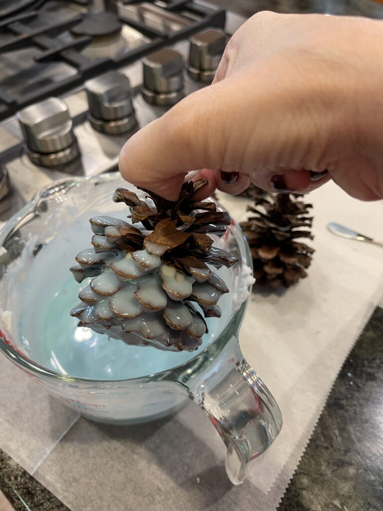 pinecone being dipped in light blue wax