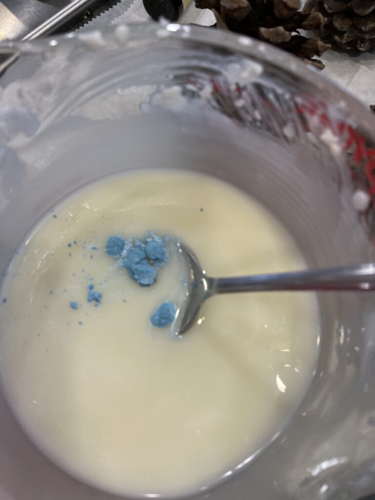 bowl of melting cream colored wax with some blue powder floating in it