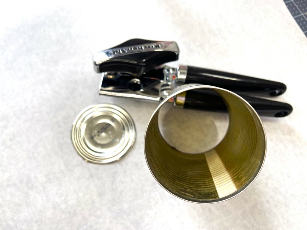 tin can with top and bottom cut out, top of can laying next to can, black hand can opener