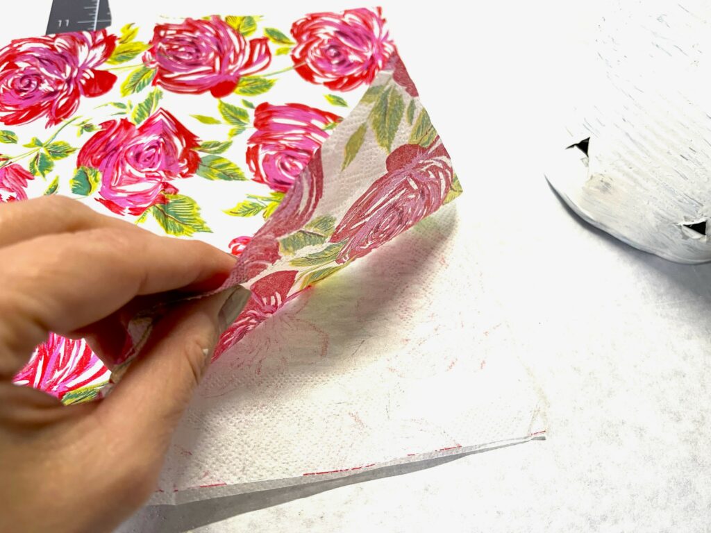 a hand separating the layers of a paper napkin, with pink roses and green leaves on the napkin