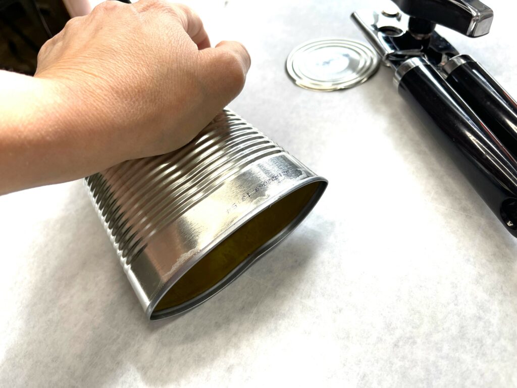 a hand pushing down on empty tin can to flatten it, a lid of a can and a black hand can-opener