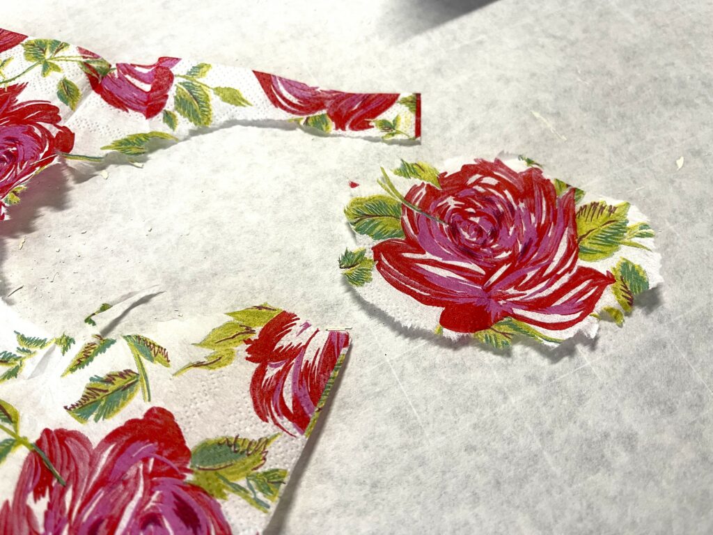 a paper napkin with pinkish red roses and green leaves, and one of the roses has been torn away from the napkin